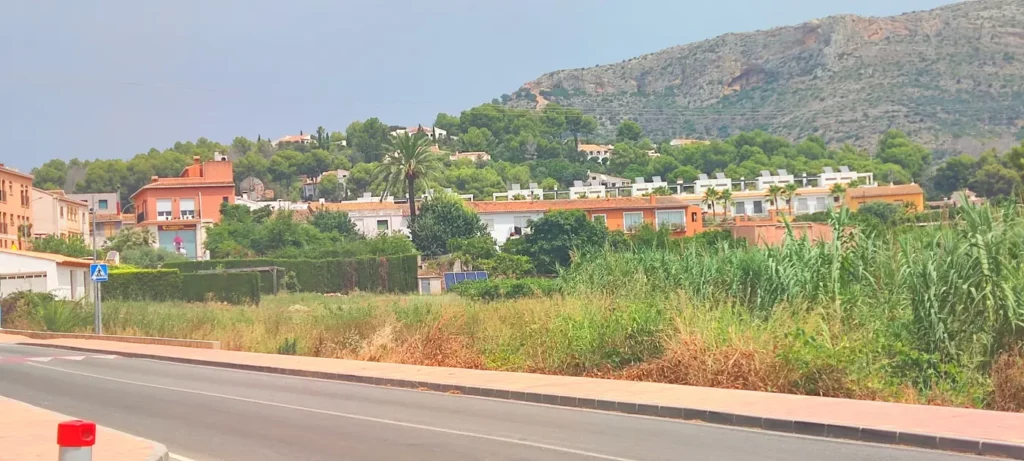 Entrada al pueblo de Jesús Pobre con carretera, casas de colores, vegetación y el Montgó al fondo.